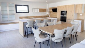 Een moderne keuken met een centraal kookeiland, inbouwapparatuur en een eethoek met grijze gestoffeerde stoelen.