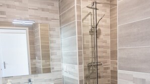 Een moderne badkamer met een douche met glazen wand, een houten wastafelmeubel en een witte wasbak.