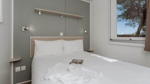 Une chambre à coucher avec un lit, une fenêtre donnant sur des arbres, une table de chevet et une étagère fixée au mur.