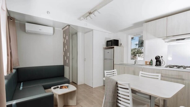 Un espace de vie moderne et compact comprenant un canapé, une petite table basse et une table à manger avec des chaises. On aperçoit également un coin cuisine équipé d’un four à micro-ondes, d’un réfrigérateur et d’une cuisinière.