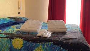 A bed with a colorful bedspread, two neatly folded towels, and red curtains. - NATIONAL GALLERY TAORMINA ROOMS WITH PRIVATE BATHROOM SHARED KITCHEN AND BALCONY (Taormina)