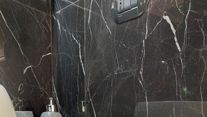 A bathroom with a white countertop, black marble walls, and various toiletries including bottles and containers. - NATIONAL GALLERY TAORMINA ROOMS WITH PRIVATE BATHROOM SHARED KITCHEN AND BALCONY (Taormina)