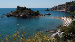 A coastal beach with rocky outcrops, clear blue sea, and a row of beach umbrellas. - NATIONAL GALLERY TAORMINA ROOMS WITH PRIVATE BATHROOM SHARED KITCHEN AND BALCONY (Taormina)
