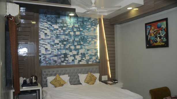 A hotel room with a bed, a nightstand, a coffee maker, and a painting on the wall. - HOTEL  RAJ PALACE SHIVPURI (Shivpuri)