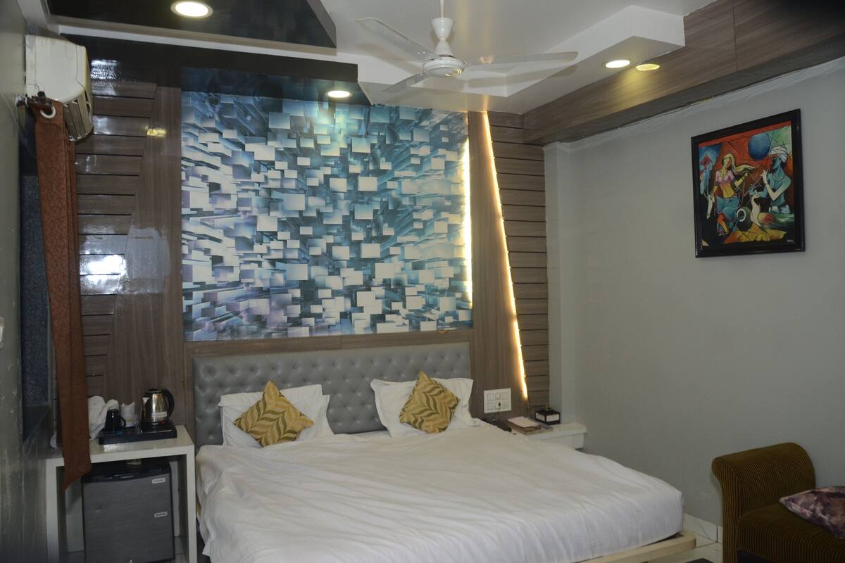 A hotel room with a bed, a nightstand, a coffee maker, and a painting on the wall.