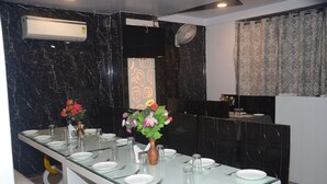 A dining area with a long table set for a meal, a vase with flowers, and a black marble wall. - HOTEL  RAJ PALACE SHIVPURI (Shivpuri)