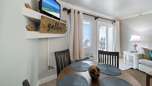 Ein Essbereich mit Fernseher, Holzböden, einem Schild mit der Aufschrift 'Gather' und Blick durch ein Fenster.