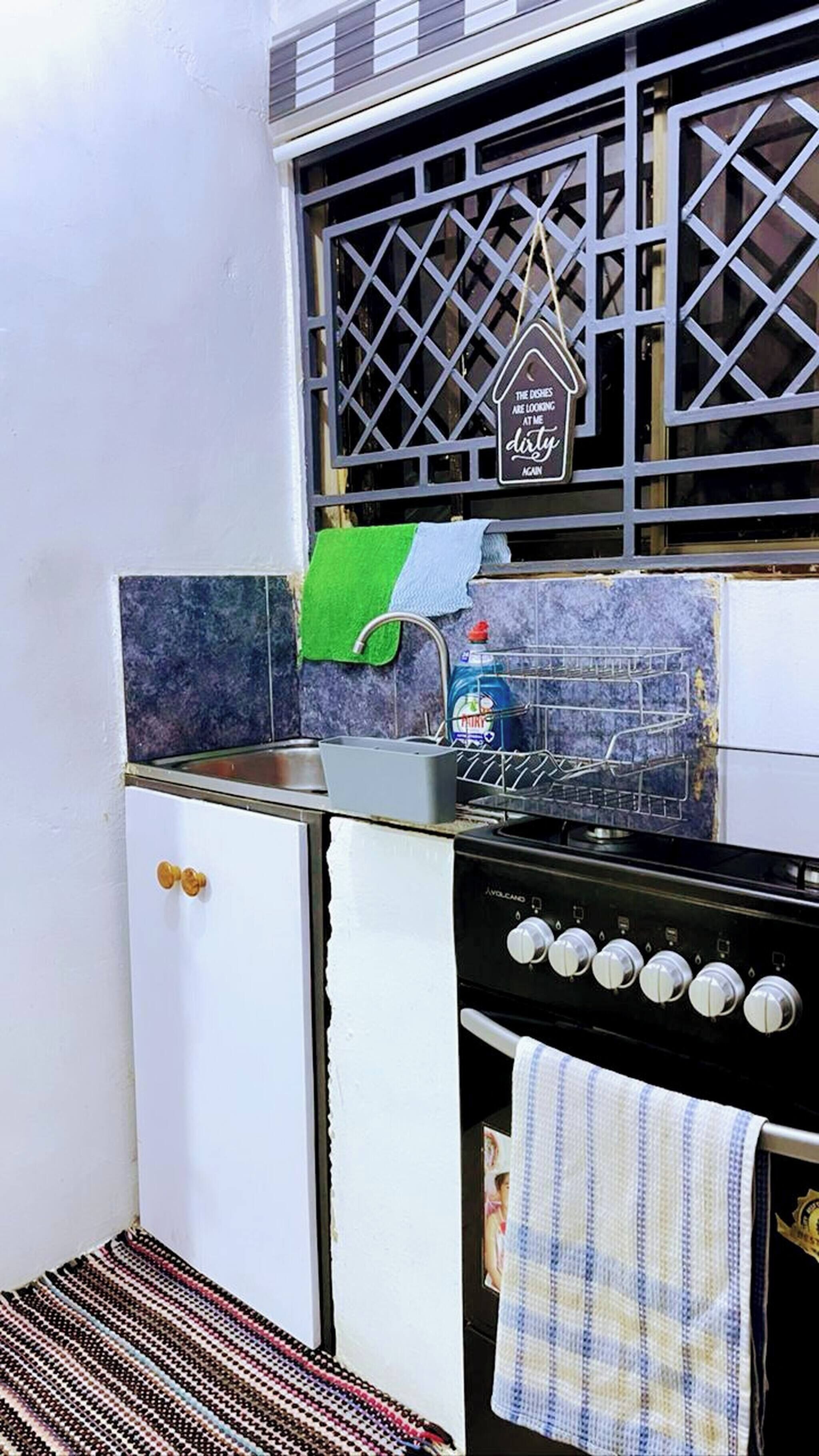 Una cocina compacta con un refrigerador blanco, una estufa con varios fuegos, un lavamanos con una toalla verde y una ventana con un letrero decorativo.