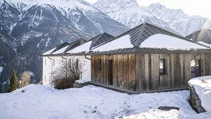 Eine Holzhütte mit einem Metall-Dach, umgeben von schneebedeckten Bergen.