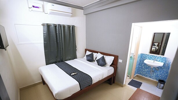 A bedroom with a bed, a bedside table, a window with curtains, and an air conditioning unit. - Blessing Select DLF (Chennai)