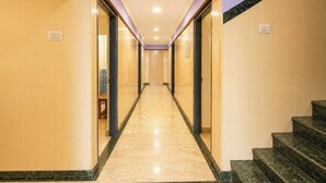 A hotel hallway with a marble floor, doors on both sides, and a staircase on the right. - Blessing Select DLF (Chennai)