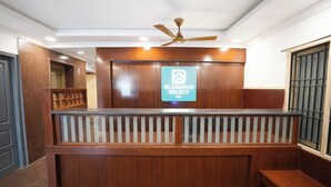 A reception area with a wooden reception desk, a ceiling fan, and a sign indicating 'Blessings Select DLF'. - Blessing Select DLF (Chennai)