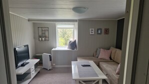 A room with a TV, a radiator, a window with a view, a sofa, and a table. - Quaint 1-bedroom basement apartment in charming Vestland (Vestland)