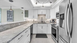 Una cocina moderna con armarios blancos, un refrigerador de acero inoxidable, horno integrado y encimera de granito.