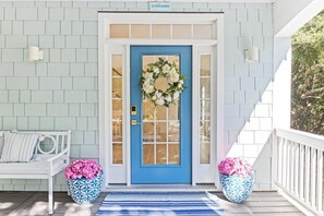 A blue door with a wreath, white bench, and two potted plants on a porch. - "One Particular Harbor" BHI and Shoals Club, 5 BR 3.5 BA, New Rental 2026 (Bald Head Island)