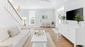A spacious living room with a white sofa, a coffee table, and a TV mounted on the wall. - "One Particular Harbor" BHI and Shoals Club, 5 BR 3.5 BA, New Rental 2026 (Bald Head Island)