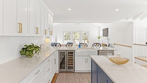 A modern kitchen with white cabinetry, a central island, and a view of the outdoors through large windows. - "One Particular Harbor" BHI and Shoals Club, 5 BR 3.5 BA, New Rental 2026 (Bald Head Island)
