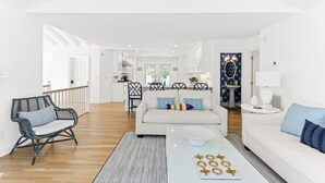 A spacious living room with a white sofa, a coffee table with a board game, and a dining area with chairs and a table. - "One Particular Harbor" BHI and Shoals Club, 5 BR 3.5 BA, New Rental 2026 (Bald Head Island)