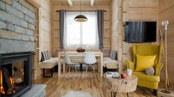 A cozy log cabin interior with a fireplace, a dining area, a yellow armchair, and a television mounted on the wall.