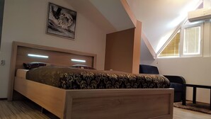 Un dormitorio con cama de madera, cabecero con iluminación integrada, ventana grande con persianas y un cuadro en la pared.