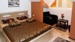 Un dormitorio con una cama grande, un escritorio, una silla, una mesita con flores y una ventana con persianas.