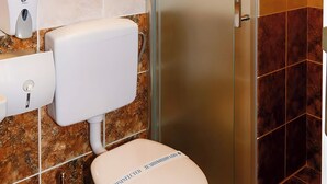 Un baño con inodoro, secamanos y cabina de ducha con paredes de vidrio.