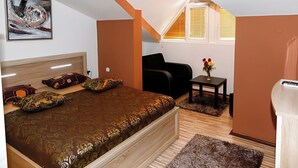 Un dormitorio con una cama, una silla negra, una mesita con un florero y una ventana con persianas.