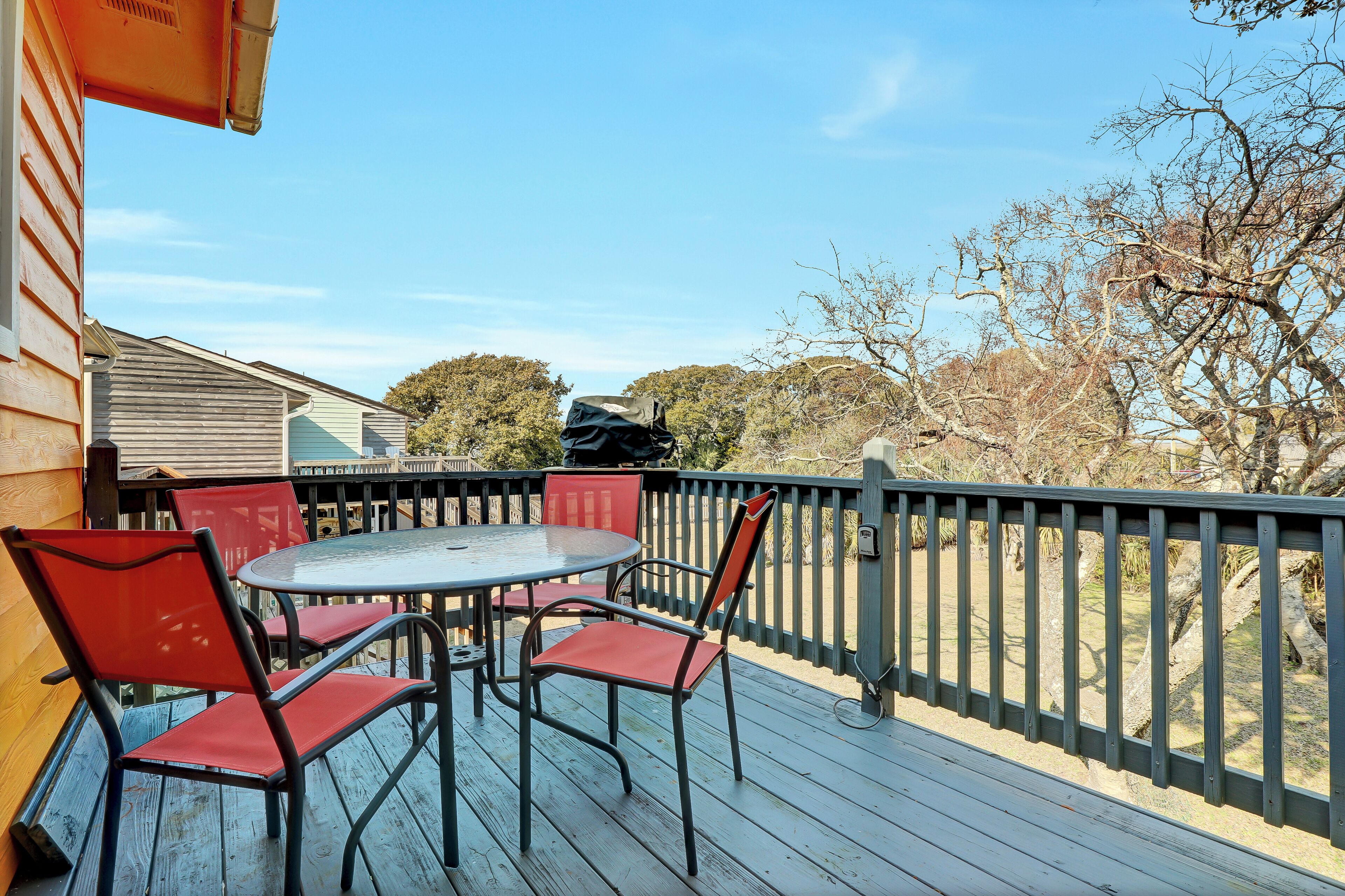 Una terraza de madera con una mesa redonda y sillas rojas, con vistas a un paisaje natural.