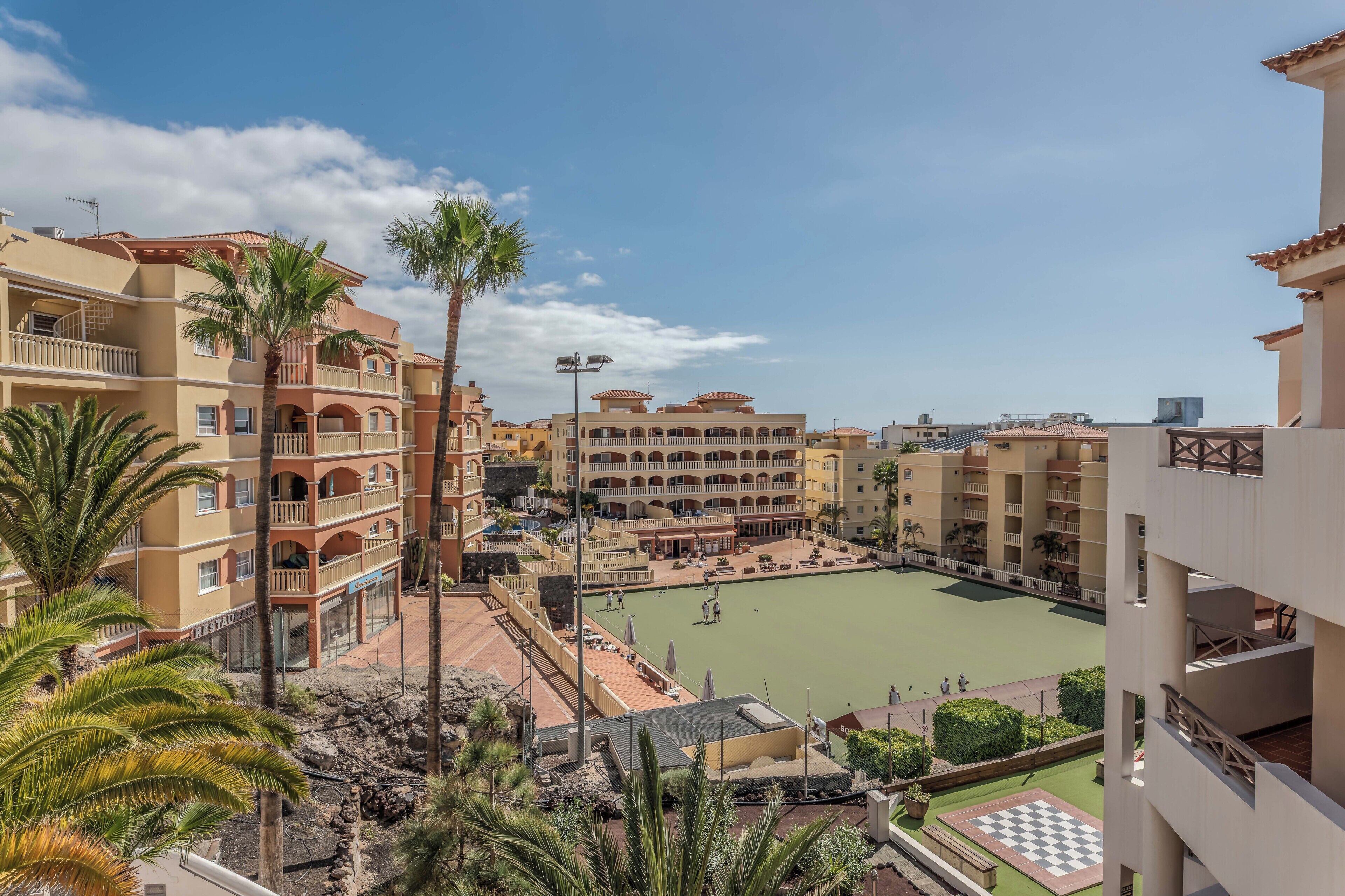 Een meerhoog hotel met balkons, een binnentuin en palmbomen.