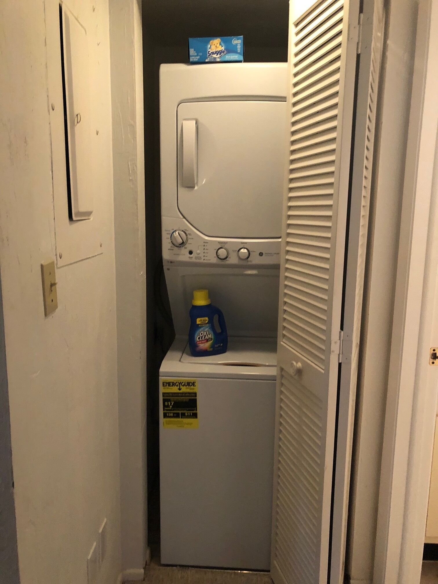 A compact, white laundry room with a built-in washer and dryer. A Snuggle brand box is placed on the dryer, and an ENERGYGUIDE sticker is visible on the washer.