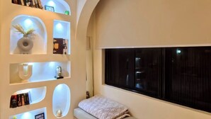 Un rincón acogedor para leer con un banco acolchado, un ventanal grande y estanterías empotradas con libros y objetos decorativos.