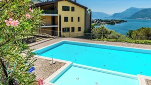 A swimming pool with a view of a lake and mountains, a yellow building with balconies, and a clear sky. - Lake View Penthouse by Interhome (Dervio)
