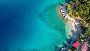 An aerial view of a coastal area with clear turquoise waters, a sandy beach, and several buildings with red roofs. - Apartment Vesna by Interhome (Krk/Pinezići)