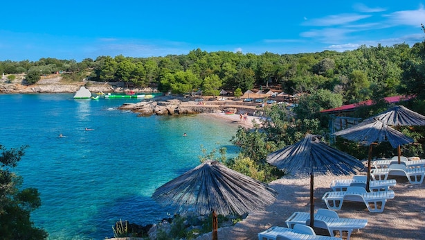 A coastal beach with clear blue waters, beach umbrellas, and lounge chairs. - Apartment Vesna by Interhome (Krk/Pinezići)