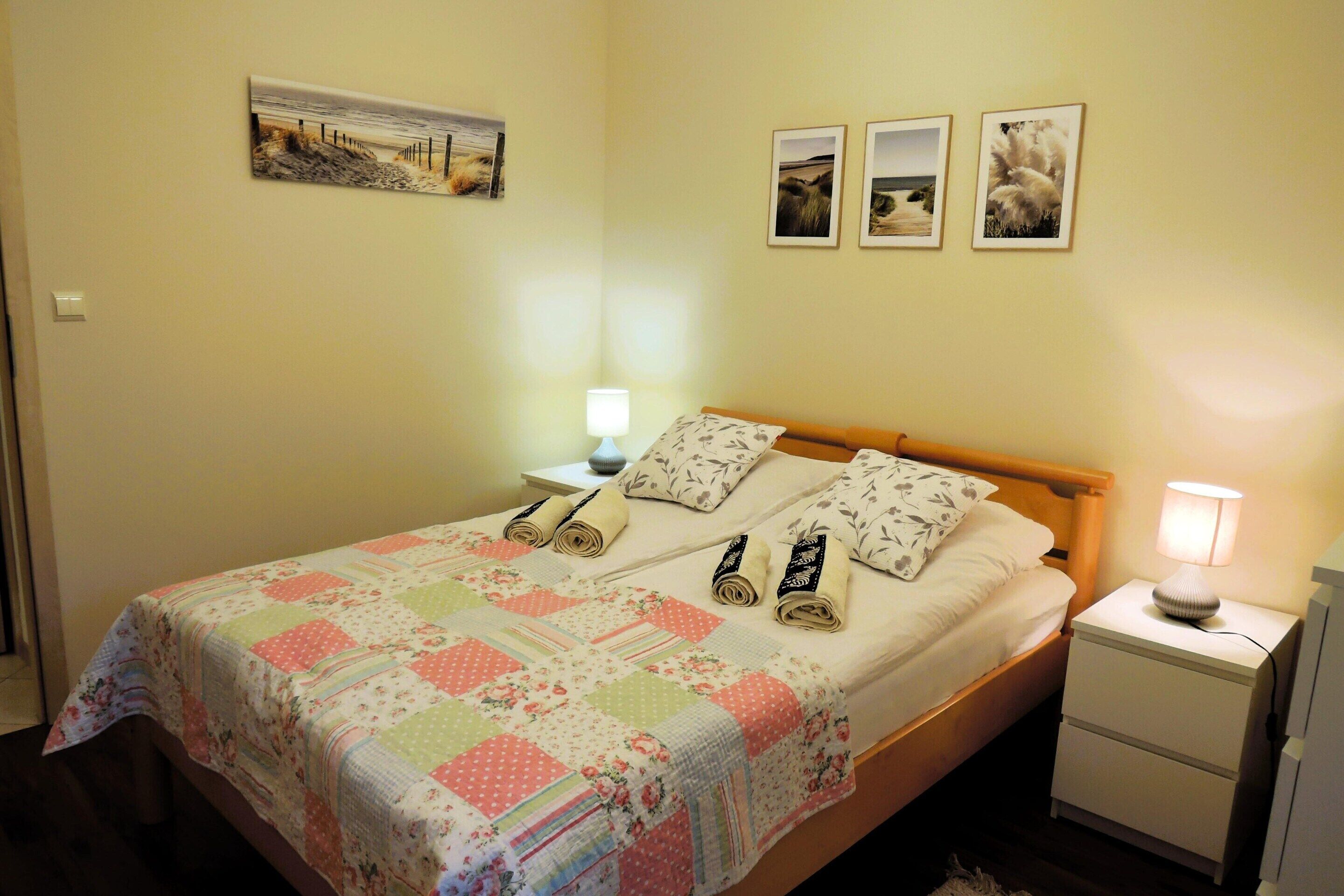 A neatly made bed with a floral quilt, two bedside lamps, and a nightstand with a lamp.