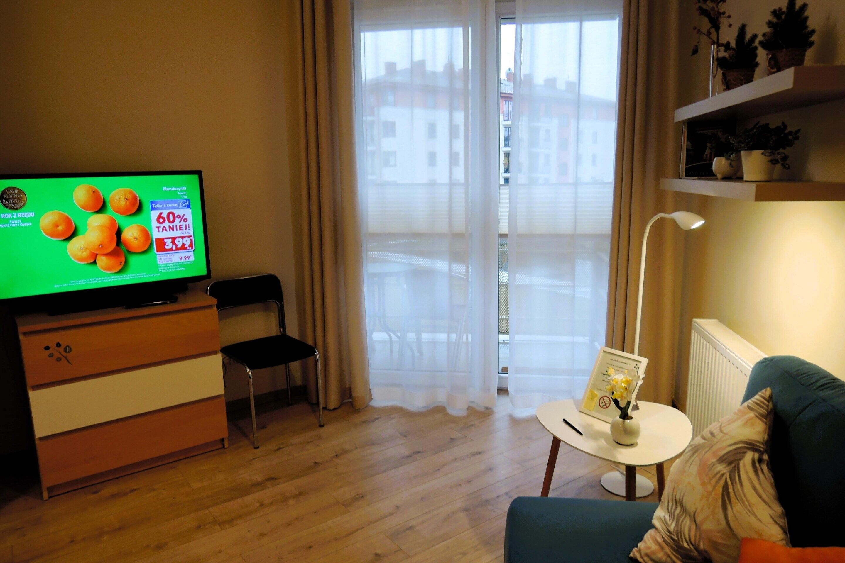 Ett vardagsrum med en tv-apparat som visar en orangefärgad reklamfilm, ett litet bord med en vas, en soffa och en stol.