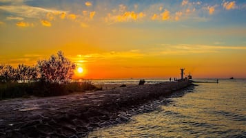 Un coucher de soleil sur une plage, avec un moulin à vent et un navire à l’horizon.