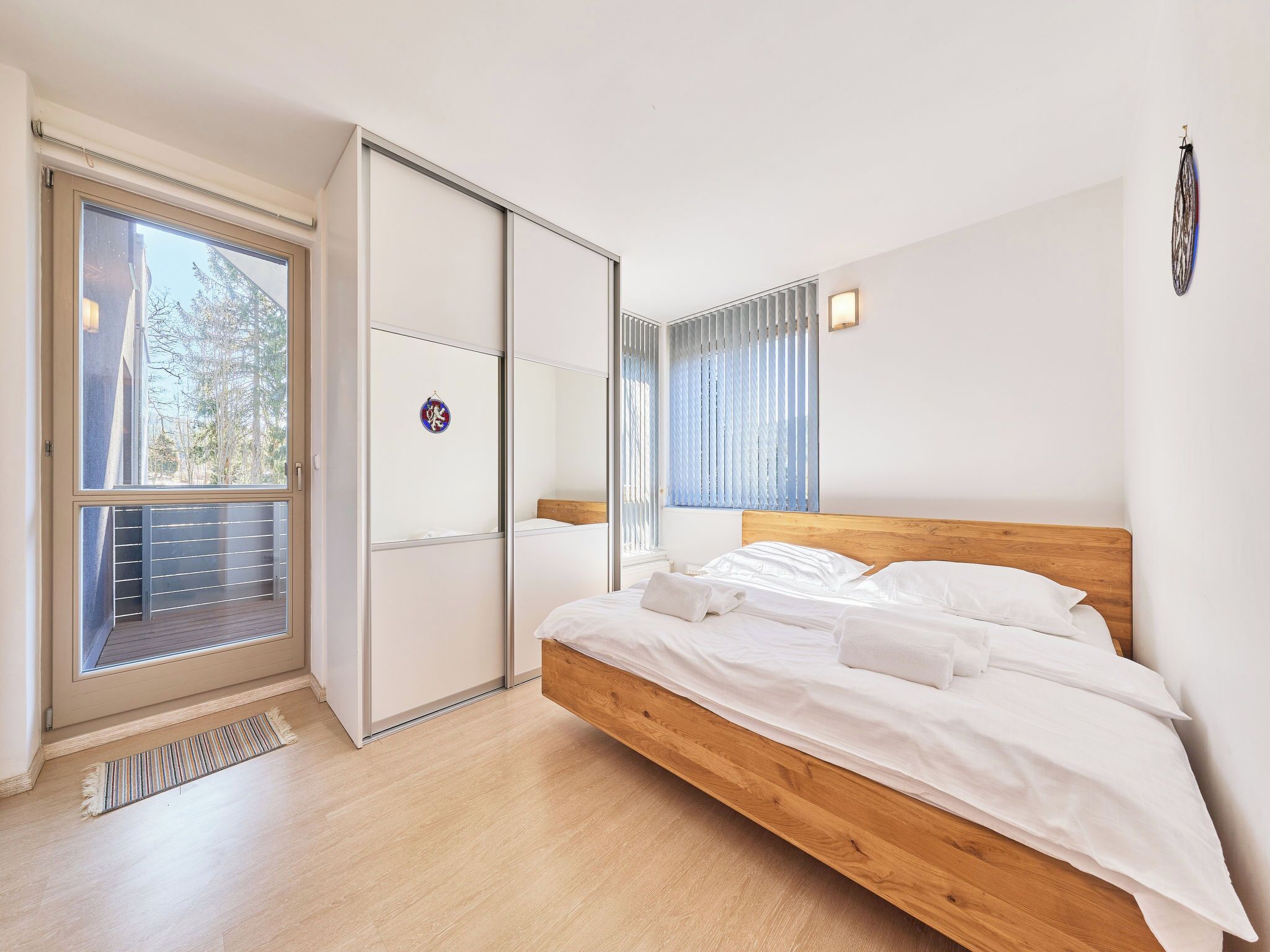 A bedroom with a wooden bed, a sliding door closet, a small window with blinds, and a view of the outdoors.