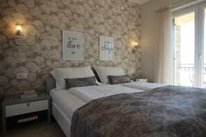 Ein Schlafzimmer mit blumigem Wandpapier, zwei Nachttischen, einem Bett mit grauer Decke und zwei Wandleuchten.