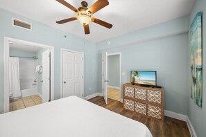 Ein Schlafzimmer mit Bett, Deckenventilator, Fernseher und einem Badezimmer mit Dusche und Toilette.