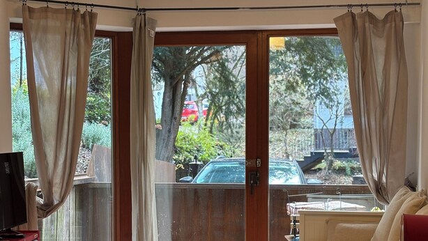 A dining area with a wooden table and chairs, a television on a red stand, and a view of the outside through a glass door with curtains. - Vacation apartment on the Moselle (Koblenz)