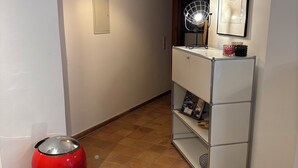 A hallway with a red trash bin, a white shelving unit, and a hanging light fixture. - Vacation apartment on the Moselle (Koblenz)