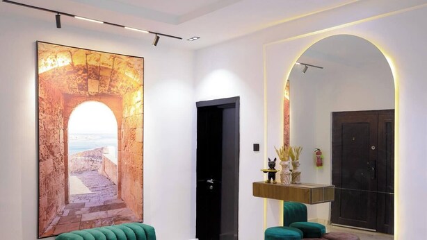 A modern interior with a large abstract painting, a green sofa, a mirror with a circular frame, and a wooden console table. - Decobel Apartment (Abuja)