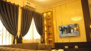 A modern living room with a sofa, a small round table, and a television mounted on the wall. - Decobel Apartment (Abuja)