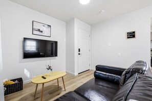 Ein modernes Wohnzimmer mit einer schwarzen Ledersofa, einem Holztisch, einem flachbildfernseher an der Wand und einer Tür mit einem Willkommensschild.
