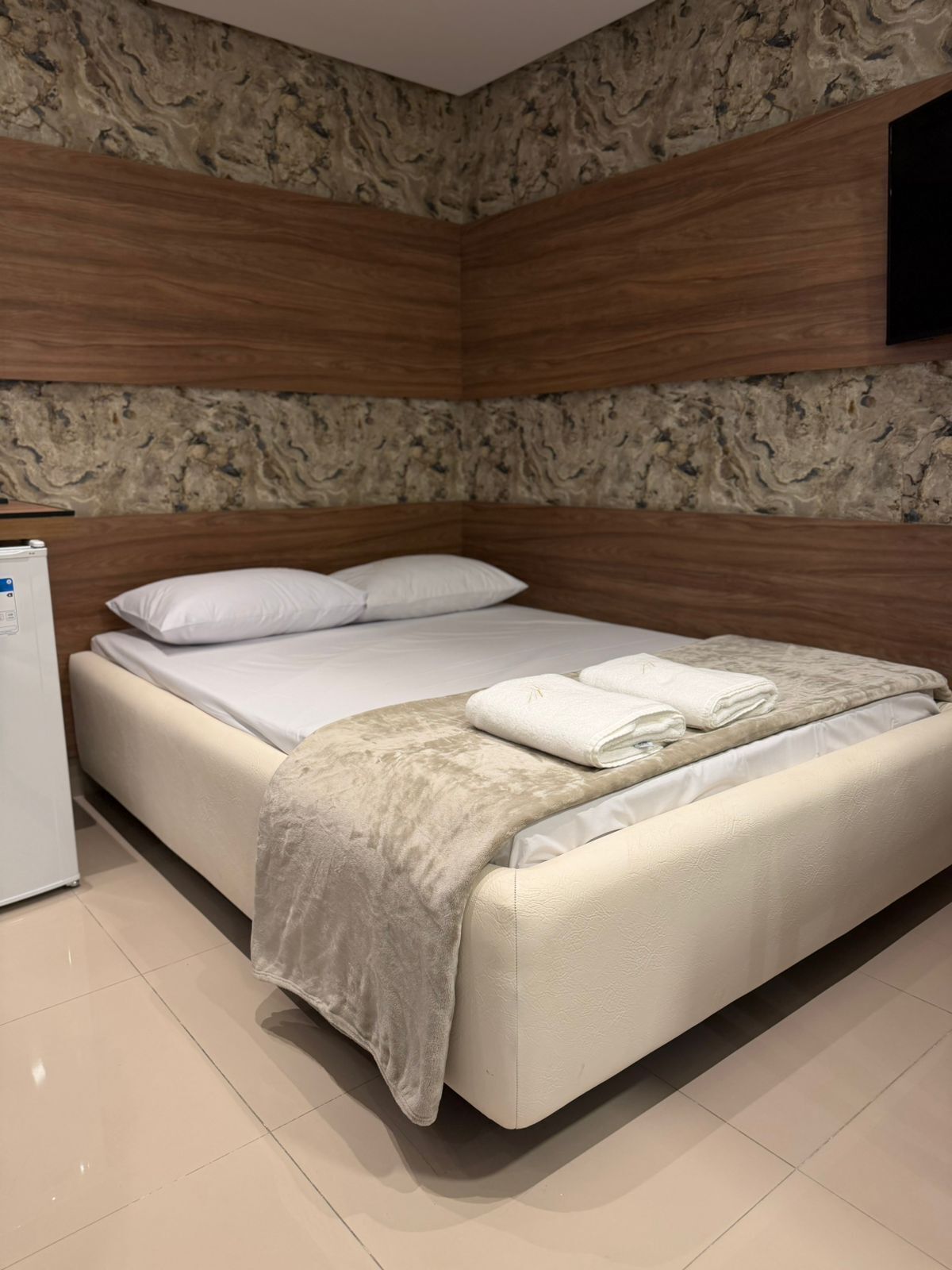 Un dormitorio con cama, almohadas, una colcha y un televisor de pantalla plana montado en la pared.