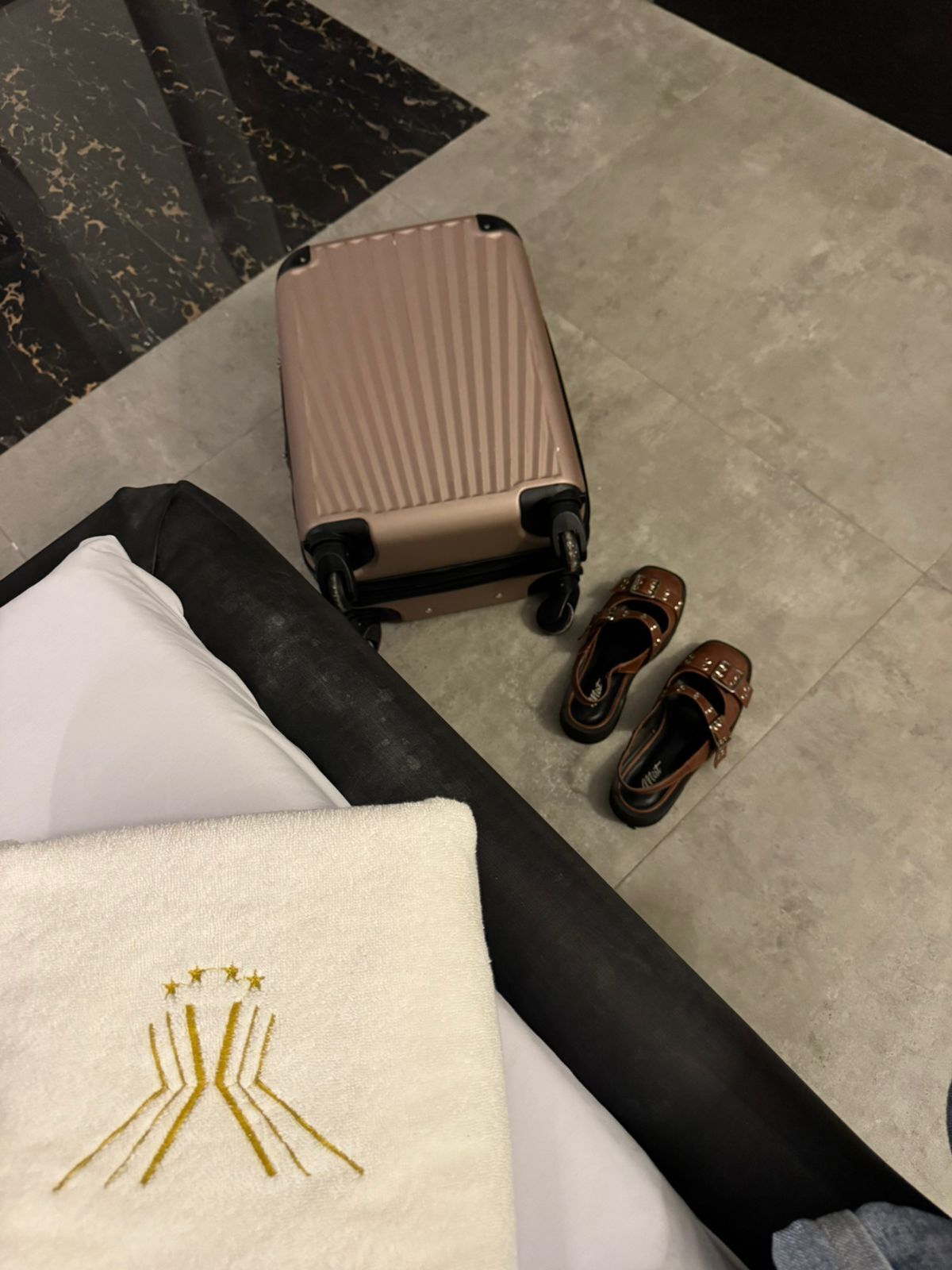 Una habitación con una maleta grande, un par de zapatos y una almohada con bordado de estrella.