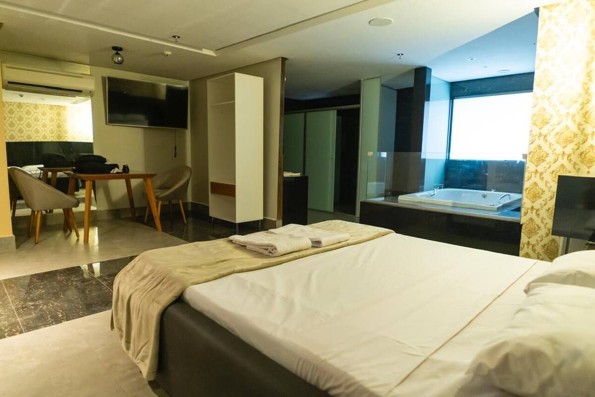 A hotel room with a bed, a desk, a chair, a TV, and a bathtub.