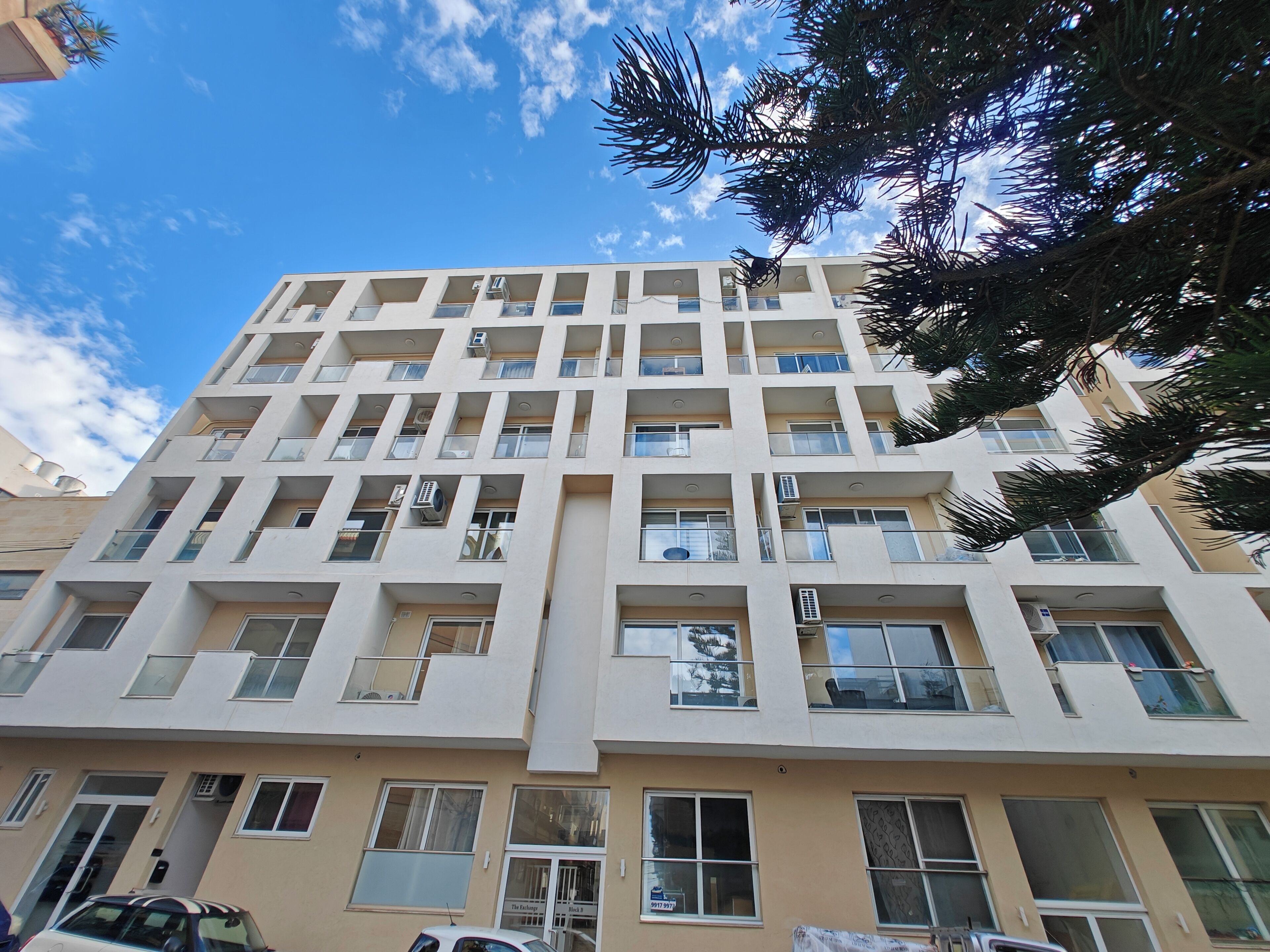 A multi-story building with balconies, air conditioning units, and a clear sky.