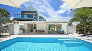 Ein modernes Haus mit Swimmingpool, Sitzgelegenheiten im Freien und einer überdachten Terrasse.